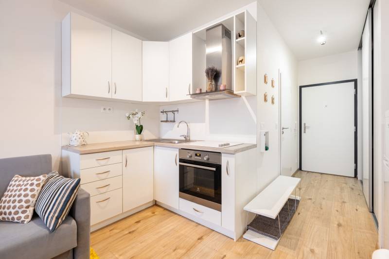 Prenájom 1-izbového bytu, Béžová, Béžová, Petržalka - REZERVOVANÉ - Kuchyňa s bielymi skrinkami v 1-izbovom byte a podlahou s dreveným dekorom.