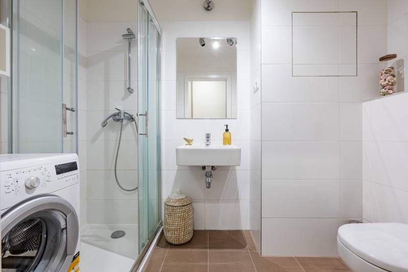 Prenájom 1-izbového bytu, Béžová, Béžová, Petržalka - REZERVOVANÉ - Kúpeľňa v 1-izbovom byte s práčkou, sprchovým kútom a bielymi obkladmi.