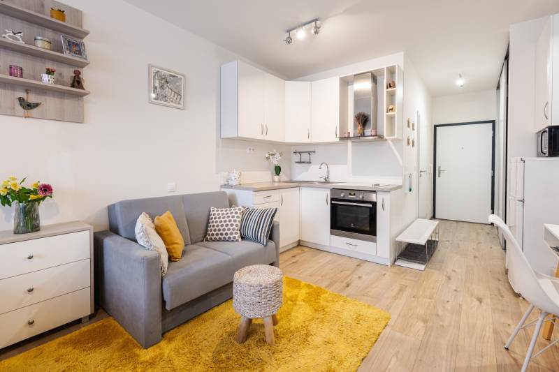 Prenájom 1-izbového bytu, Béžová, Béžová, Petržalka - REZERVOVANÉ - Kompaktný 1-izbový byt s kuchynským kútom, sivou pohovkou a podlahou s dreveným dekorom.