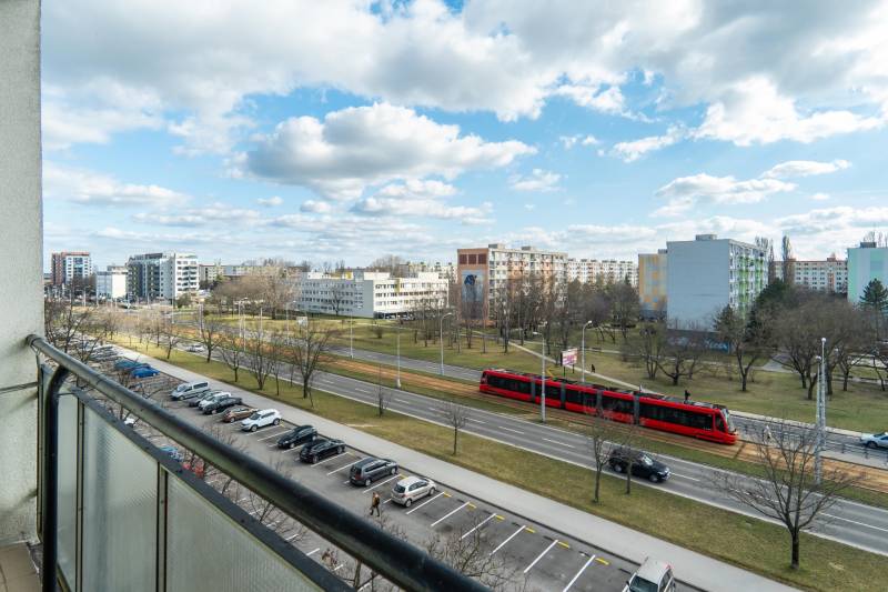 Komfortný 1,5-izbový byt s balkónom v Ružinove na predaj - Výhľad z balkóna v Bratislave - Ružinove na ulici Súmračná s električkou a parkom.