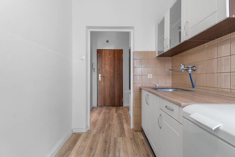 Komfortný 1,5-izbový byt s balkónom v Ružinove na predaj - Kuchyňa v 1-izbovom byte s podlahou s dreveným dekorom a bielou linkou.
