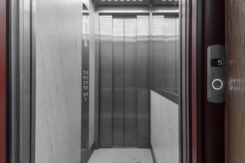 Komfortný 1,5-izbový byt s balkónom v Ružinove na predaj - Šedý výťah s kovovou kabínou a ovládacím panelom.