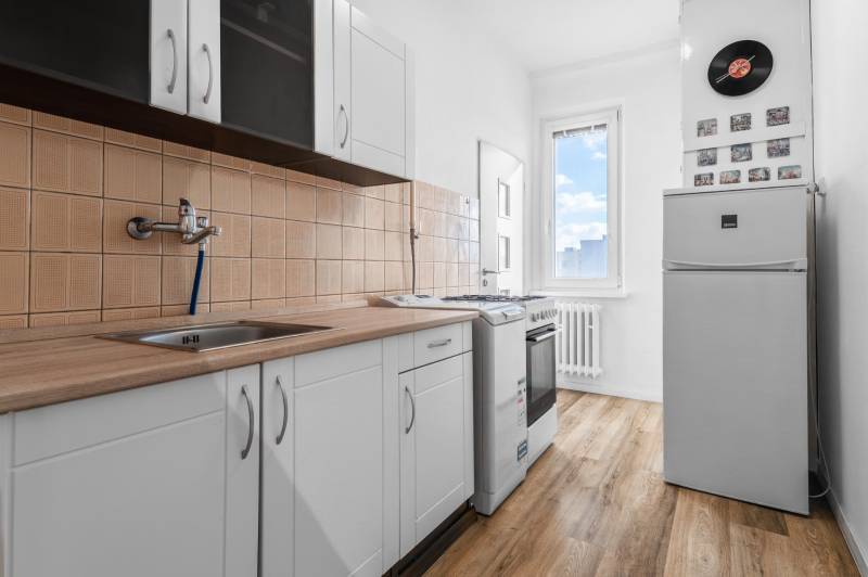 Komfortný 1,5-izbový byt s balkónom v Ružinove na predaj - Kuchyňa v 1-izbovom byte s podlahou s dreveným dekorom a bielymi skrinkami.