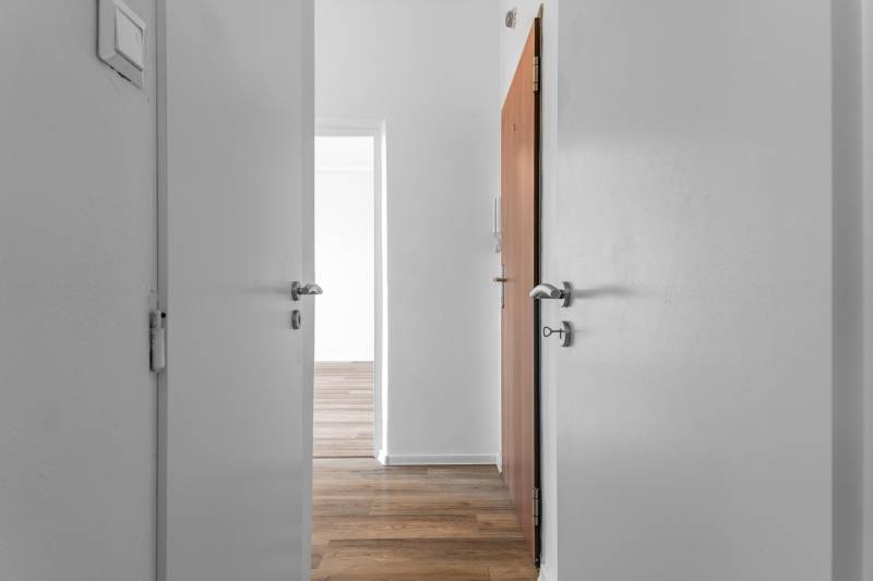 Komfortný 1,5-izbový byt s balkónom v Ružinove na predaj - Biely interiér 1-izbového bytu s podlahou s dreveným dekorom a otvorenými dverami.