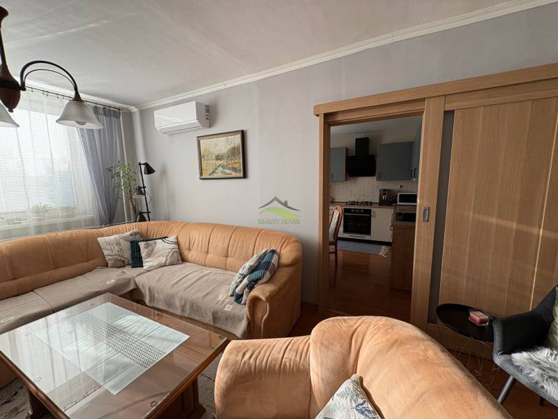 Vkusný 3 izb. byt po kompl. rekonštrukcii - Jilemnického ulica -72m2 - Obývacia izba s pohovkou, skleneným stolom a kuchyňou v 3-izbovom byte.