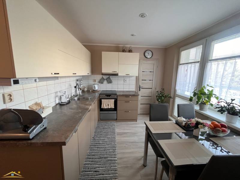 Na predaj  3-izbový byt v meste Rajec  - Kuchyňa v 3-izbovom byte so stolom, spotrebičmi a rastlinami.