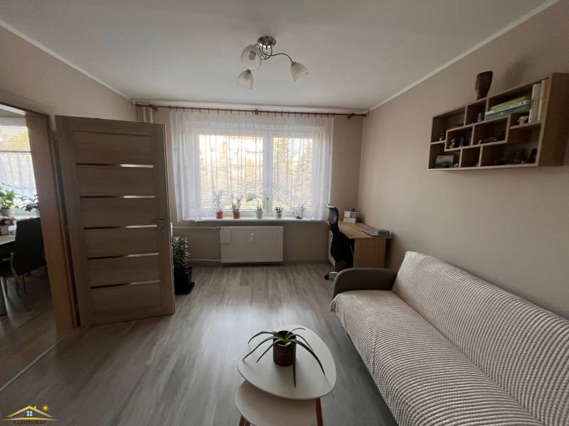 Na predaj  3-izbový byt v meste Rajec  - Obývacia izba v 3-izbovom byte s podlahou s dreveným dekorom, pohovkou a stolíkom.