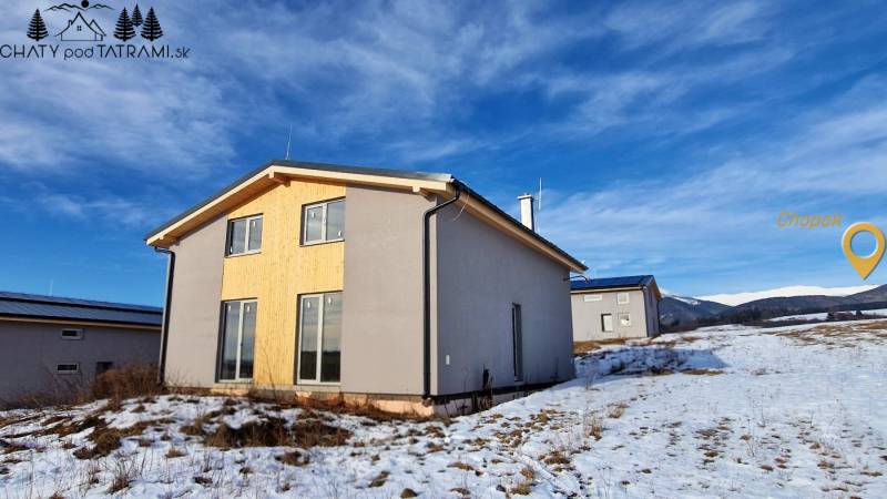 Únik z mesta, kde sa moderná architektúra stretáva s divokou prírodou? - Chata v Dolnej Lehote s dreveným obkladom, zasnežená krajina a hory na obzore.