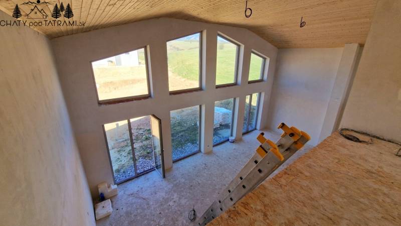 Únik z mesta, kde sa moderná architektúra stretáva s divokou prírodou? - Interiér chaty s veľkými oknami, schodíkmi a podlahou s dreveným dekorom.