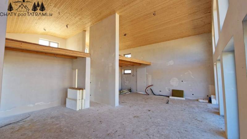 Únik z mesta, kde sa moderná architektúra stretáva s divokou prírodou? - Interiér chaty s vysokým stropom, surovo upravené steny a jemné drevené dekorácie.