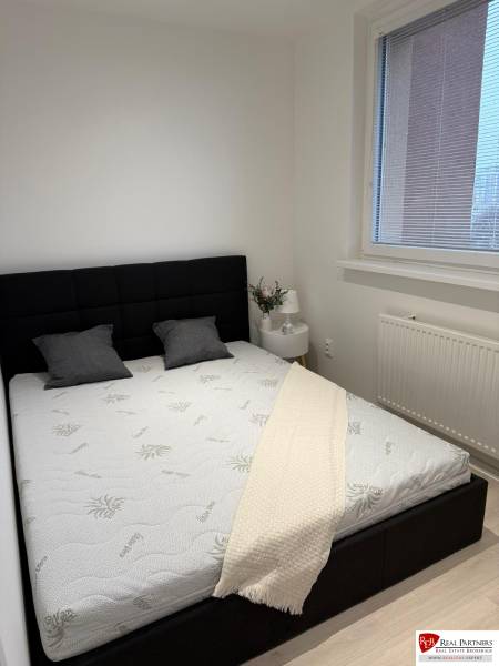 Prenájom 2-izbový byt s loggiou, 54m2, Bratislava-Petržalka - Spálňa v 2-izbovom byte s čiernym čelom postele, biela prikrývka a okno s roletami.