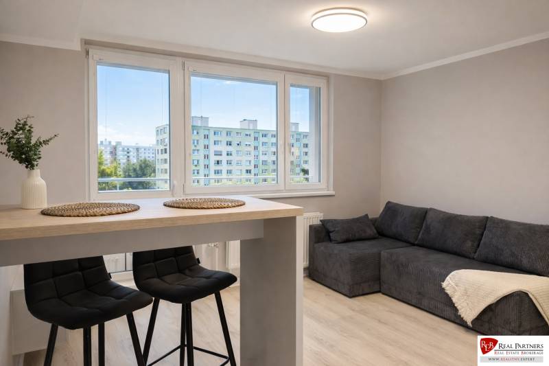 Prenájom 2-izbový byt s loggiou, 54m2, Bratislava-Petržalka - Obývacia izba v 2-izbovom byte s pohovkou, barovým stolom a stoličkami.