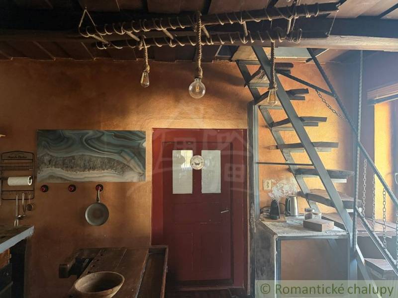 Štýlová chalupa v horskej dedinke Ratkovské Bystré - Interiér rodinného domu s drevenými schodmi, rustikálnym stolom a umeleckou maľbou na stene.