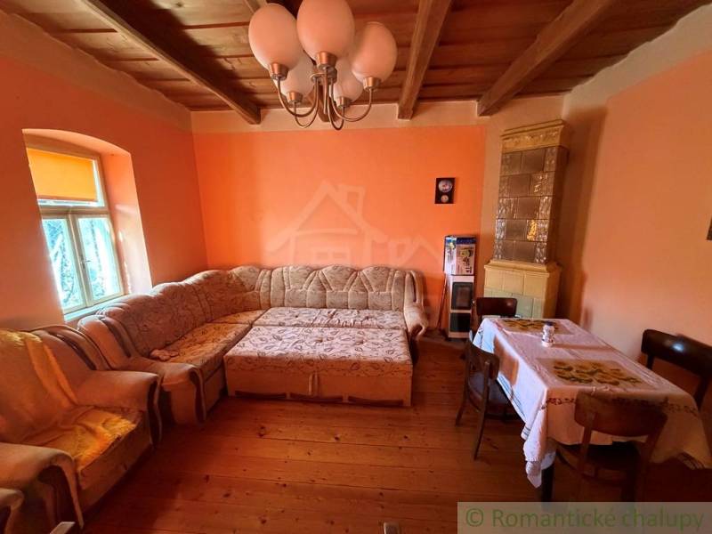 Exkluzívne: Pekná chalupa v obci Lipovec - Obývacia izba s rohovou sedačkou, podlahou s dreveným dekorom a kachľovou pecou v rodinnom dome.