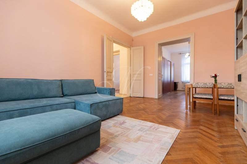 3-izbový byt s vysokými stropmi, Staré Mesto - Izba v 3-izbovom byte s modrou sedačkou, dreveným dekorom podlahy a jedálenským kútom.