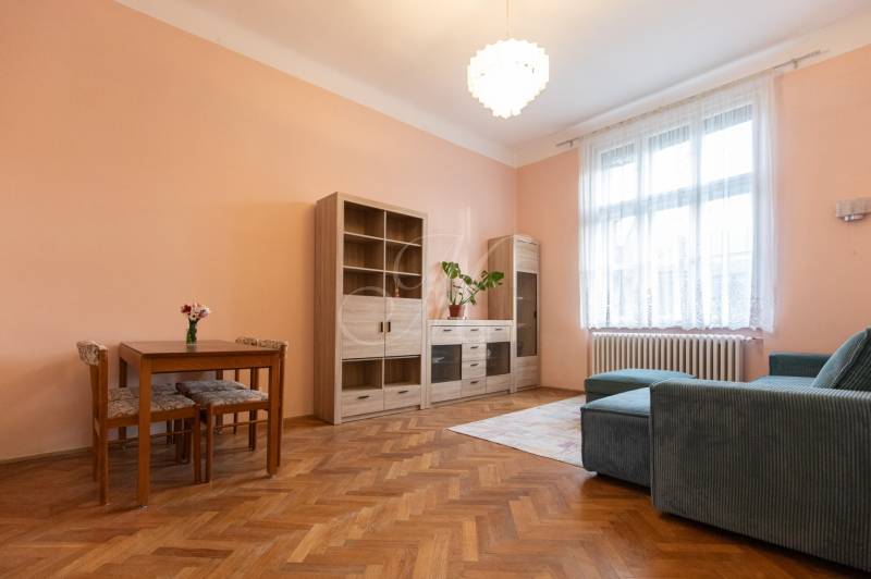 3-izbový byt s vysokými stropmi, Staré Mesto - Obývacia izba v 3-izbovom byte s podlahou s dreveným dekorom, sedačkou a nábytkom.