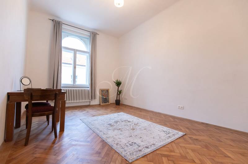 3-izbový byt s vysokými stropmi, Staré Mesto - Izba v 3-izbovom byte s podlahou s dreveným dekorom, kobercom a stolom.