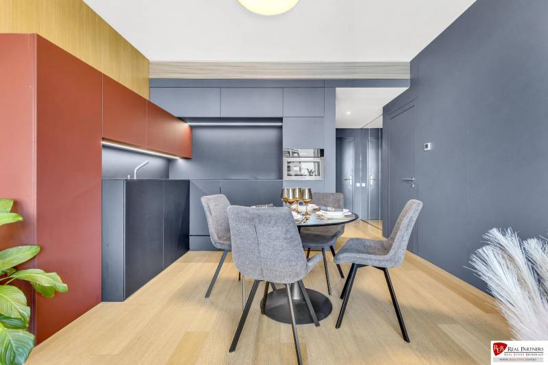 Predaj luxusný 2-izbový byt, 52 m2, Továrenská ul, SKY PARK - Moderná kuchyňa s jedálenským stolom, sivými stoličkami a podlahou s dreveným dekorom v 2-izbovom byte.