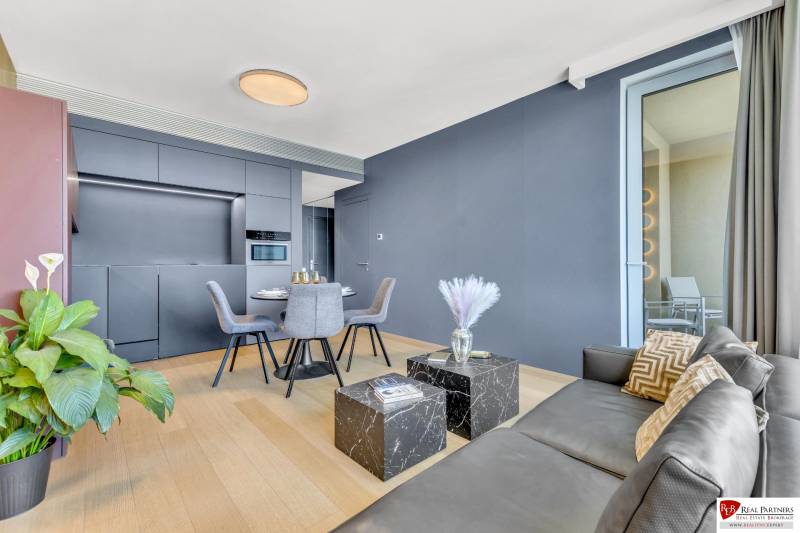 Predaj luxusný 2-izbový byt, 52 m2, Továrenská ul, SKY PARK - Obývacia izba v 2-izbovom byte s podlahou s dreveným dekorom a šedým nábytkom.