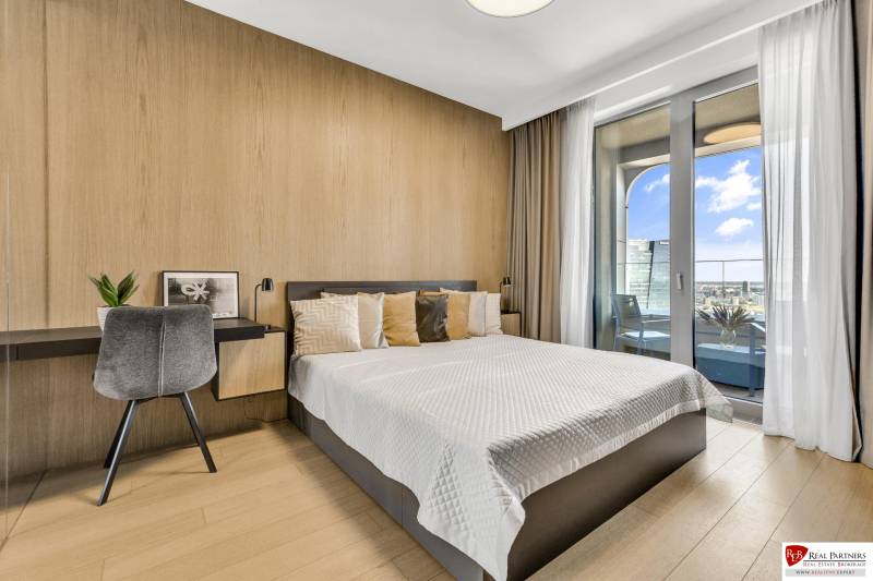 Predaj luxusný 2-izbový byt, 52 m2, Továrenská ul, SKY PARK - Spálňa s posteľou, pracovným stolom, stoličkou a balkónom v 2-izbovom byte.