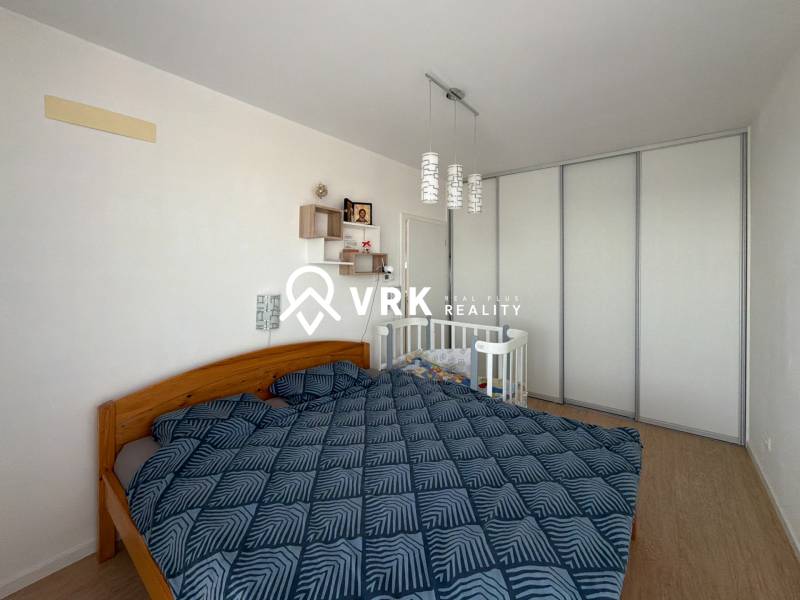 3-izbový byt s garážovým státím – Košice Západ, ul. Topoľčianska - Spálňa v 3-izbovom byte s manželskou posteľou, detskou postieľkou a podlahou s dreveným dekorom.