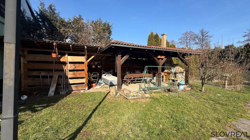 Moderný 5-izbový rodinný dom po kolaudácii 2025 | 2-generačné bývanie  - Záhrada rodinného domu v Lutile, s dreveným prístreškom a hojdačkou na pozemku.