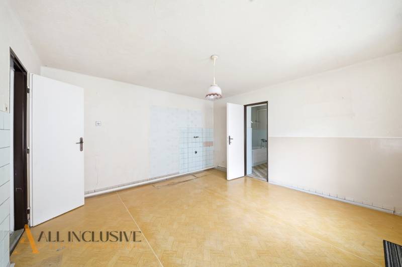 Na predaj 4-izbový rodinný dom, Topoľníky - Priestranná izba v rodinnom dome s podlahou s dreveným dekorom a jednoduchým osvetlením.