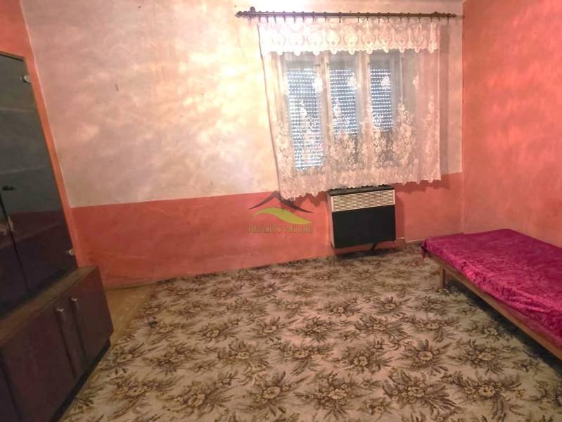 Rodinný dom v obci Pavlovce nad Uhom - Izba v rodinnom dome s kobercom, posteľou a skrinkou, záclonou na okne.