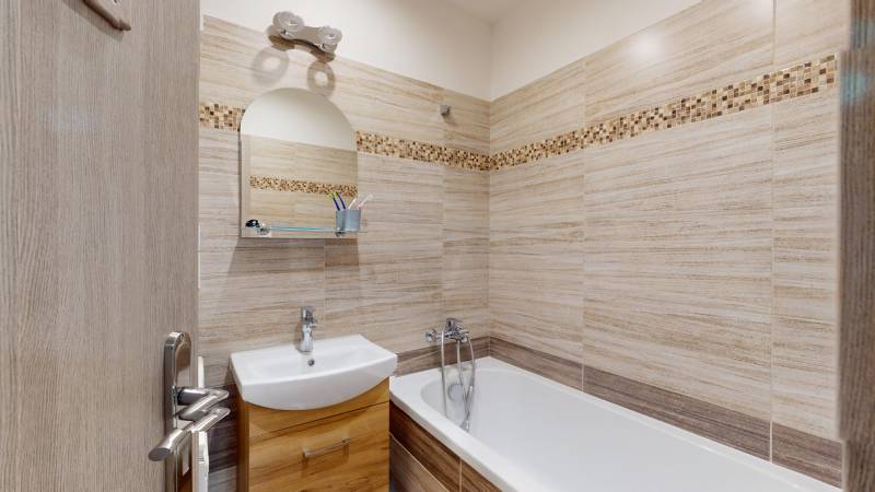 2 izbový prerobený byt v Trenčíne Pred polom, balkón + pivnica - Kúpeľňa v 2-izbovom byte so svetlými obkladmi a vaňou, skrinky pod umývadlom.