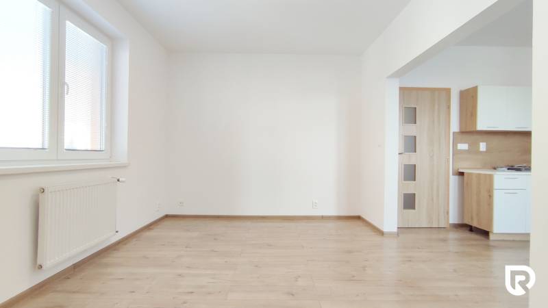 | 2-izbový byt + parking, ul. Východná | Trenčín - Obývacia izba v 2-izbovom byte s podlahou s dreveným dekorom a kuchynským kútom.