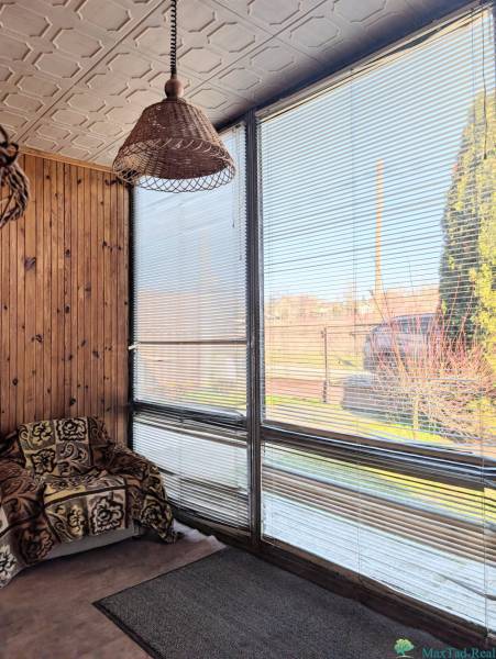 Rodinný dom s veľkou terasou a garážou v  Lastovciach za  73 500 € - Rodinný dom s ratanovou lampou, kreslom s dekou a oknami so žalúziami.