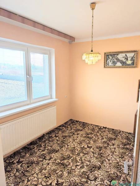 Rodinný dom s veľkou terasou a garážou v  Lastovciach za  73 500 € - V Rodinnom dome je izba s kobercovou podlahou, závesným lustrom a maľbou.