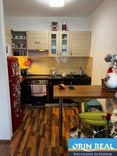 ÚTULNÝ 2 IZBOVÝ BYT - SILVANIUM  - Kuchyňa v 2-izbovom byte s drevenou podlahou, červenou chladničkou a barovým pultom.