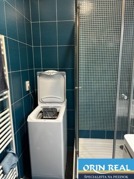 ÚTULNÝ 2 IZBOVÝ BYT - SILVANIUM  - Kúpeľňa v 2-izbovom byte so sprchou a práčkou, obklad z tmavých obkladov.