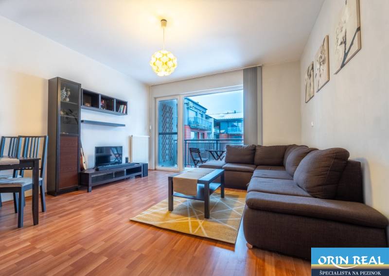 SVETLÝ ZARIADENÝ 2-IZBOVÝ BYT S BALKÓNOM - LA VITA  - Obývacia izba v 2-izbovom byte s podlahou s dreveným dekorom a sedacou súpravou.