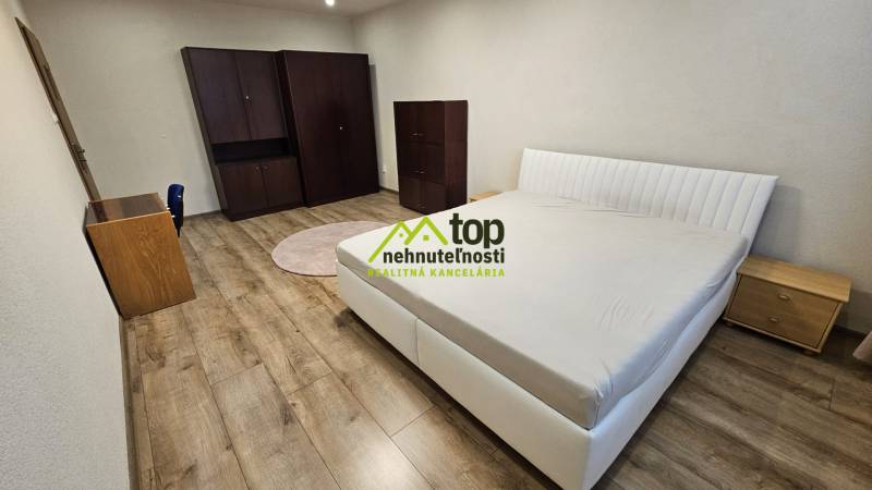 Prenájom 2 izbový byt v Topoľčanoch, sídlisko JUH - Spálňa v 2-izbovom byte s posteľou, skriňou a podlahou s dreveným dekorom.