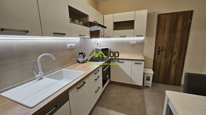 Prenájom 2 izbový byt v Topoľčanoch, sídlisko JUH - Kuchyňa v 2-izbovom byte s bielymi skrinkami a podlahou s dreveným dekorom.