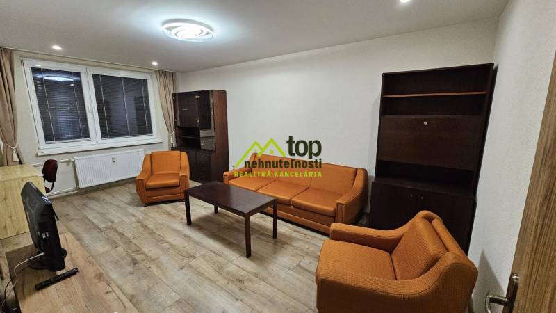 Prenájom 2 izbový byt v Topoľčanoch, sídlisko JUH - Obývacia izba v 2-izbovom byte s oranžovými sedačkami a podlahou s dreveným dekorom.