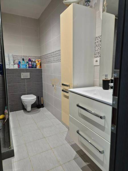 3-izb. byt v obci Blatná na Ostrove, balkón, lodžia, novostavba - Kúpeľňa v 3-izbovom byte so závesným WC, umývadlom, skrinkou a svetlými obkladmi.