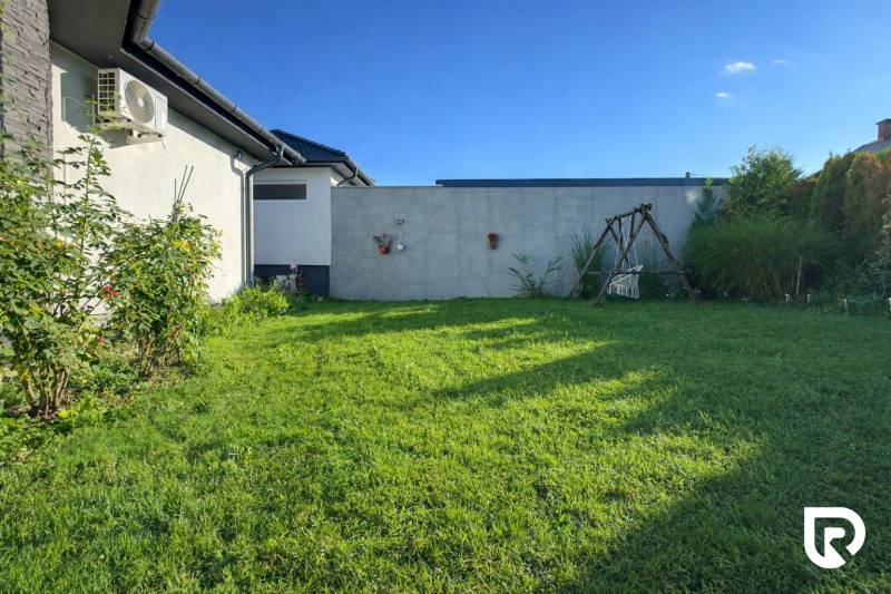 RADO I 4-IZBOVY murovaný ROD.DOM I RAJKA - Záhrada rodinného domu v Rajke s trávnikom, hojdačkou a kríkmi popri stene.