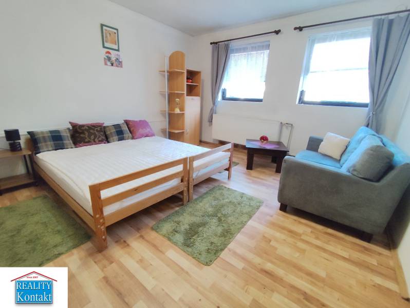 Na prenájom 1-izbový byt - Nové Zámky - V 1-izbovom byte je posteľ, pohovka a podlaha s dreveným dekorom.