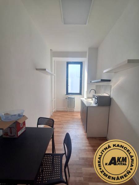 Prenájom priestoru  155 m2, Tulská ul., Zvolen-Západ - Úzka kancelária s čiernym stolom, stoličkami a podlahou s dreveným dekorom.