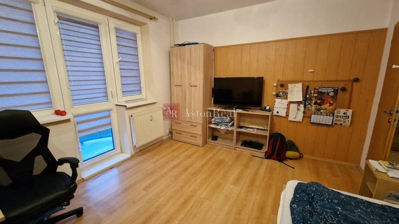 EXKLUZÍVNE-PREDAJ 3-IZBOVÝ BYT POPRAD, juh-bl.Slnečnica 80 m2  2 balk. - Izba v 3-izbovom byte s podlahou s dreveným dekorom, televízorom a kreslom.