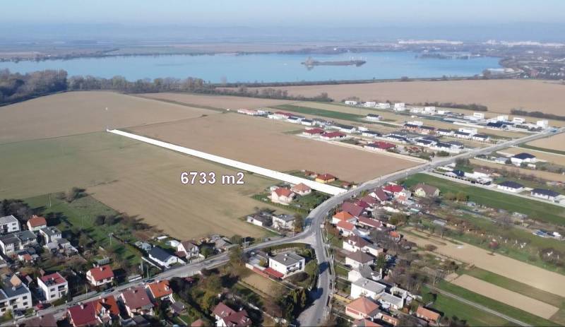 INVESTIČNÝ POZEMOK 6733 m² NA RD – SOKOLOVCE (okres Piešťany) - Pozemky na bývanie v Sokolovciach, okolitá krajina s vodnou plochou v pozadí.