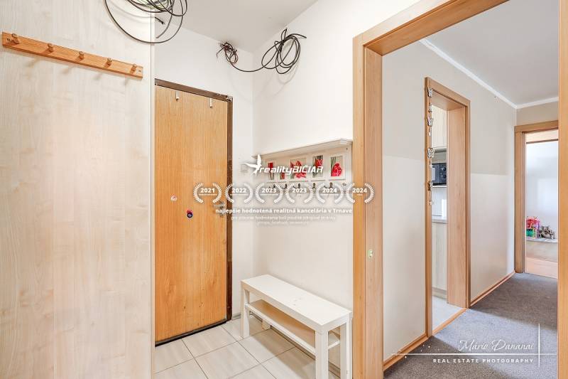 REZERVOVANÉ 4-izbový byt v Trnave na Veternej ulici - Vstupná chodba v 4-izbovom byte, biele steny, vešiaky a lavica.