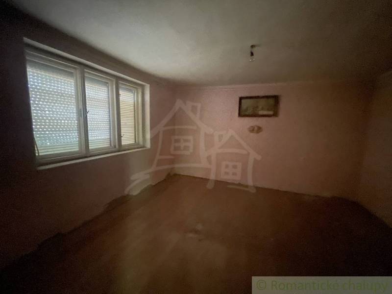 Rodinný dom v pôvodnom stave na 7 árovom pozemku v Tvrdošovciach - Prázdna izba v rodinnom dome s podlahou s dreveným dekorom a veľkým oknom.