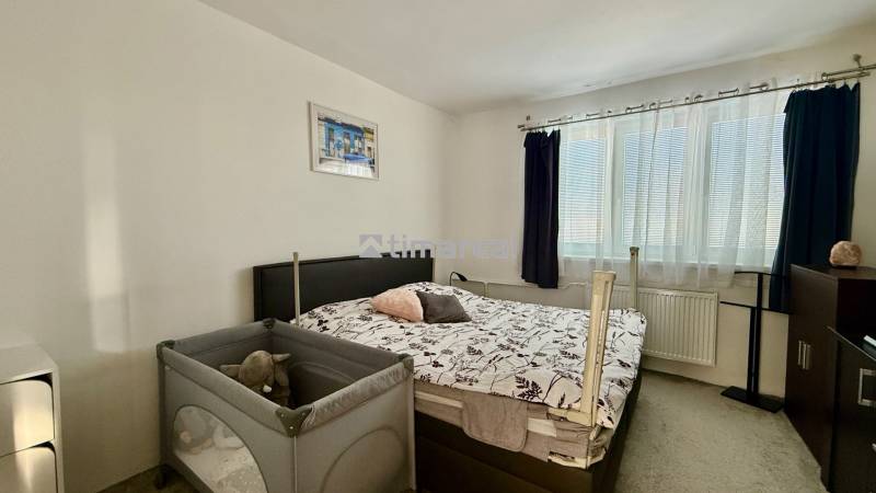 * 7i rodinný dom, veľký 33.5á pozemok, Brestovany - Spálňa v rodinnom dome s posteľou, detskou postieľkou a oknom s tmavými závesmi.