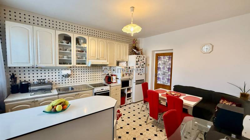 * 7i rodinný dom, veľký 33.5á pozemok, Brestovany - Kuchyňa v rodinnom dome s bielymi skrinkami, jedálenským stolom a červenými stoličkami.