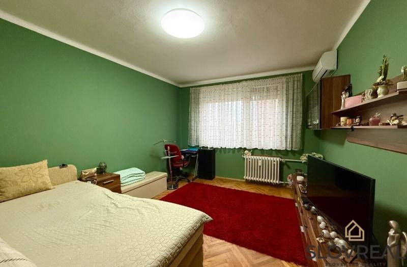 Predaj 3 - izbového bytu - Nová Baňa - Spálňa v 4-izbovom byte s posteľou, červeným kobercom a zelenými stenami.