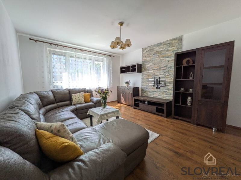 Predaj 3 - izbového bytu - Nová Baňa - Obývacia izba v 3-izbovom byte s podlahou s dreveným dekorom a veľkou sedačkou.